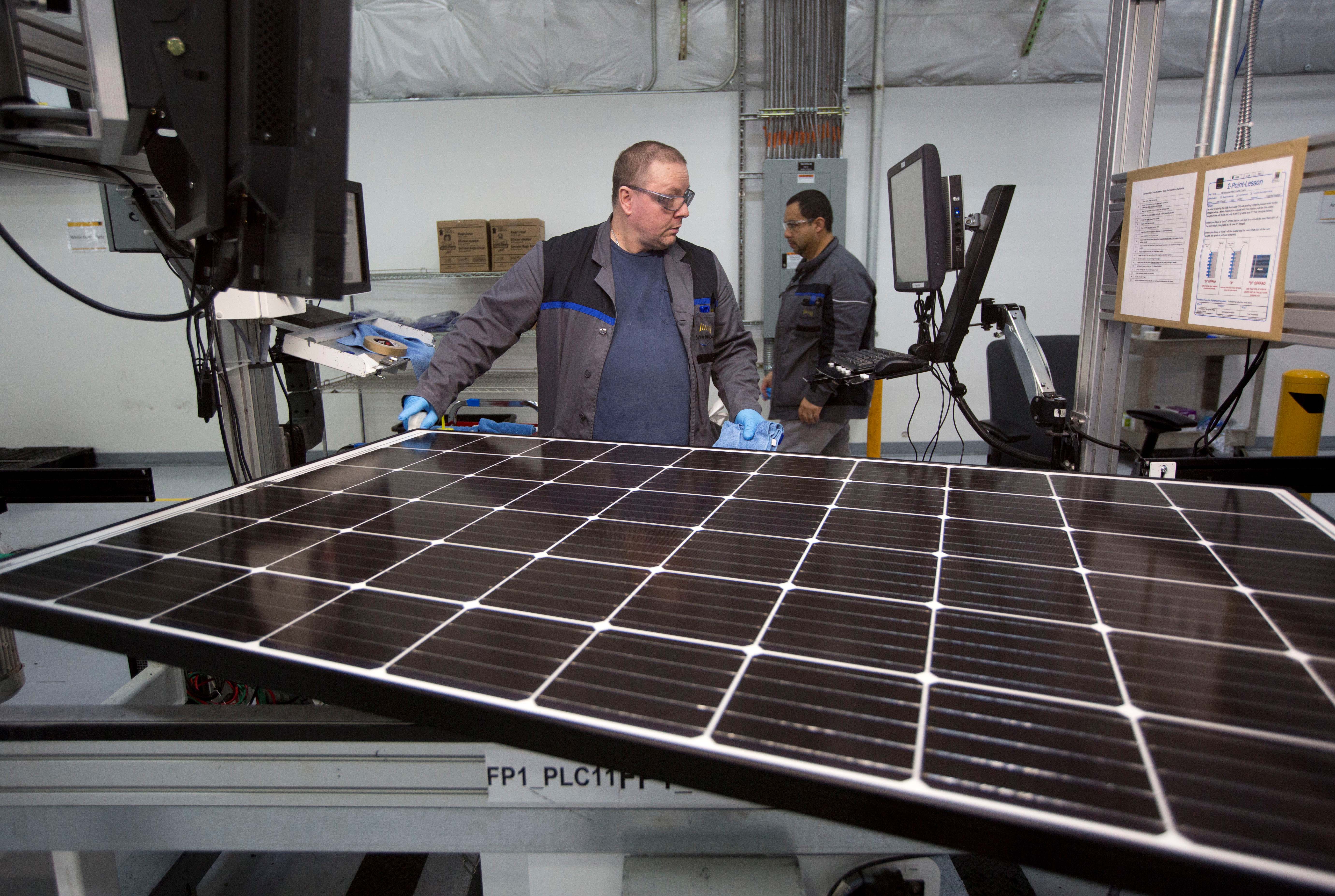 A man inspects a large solar panel within a factory.