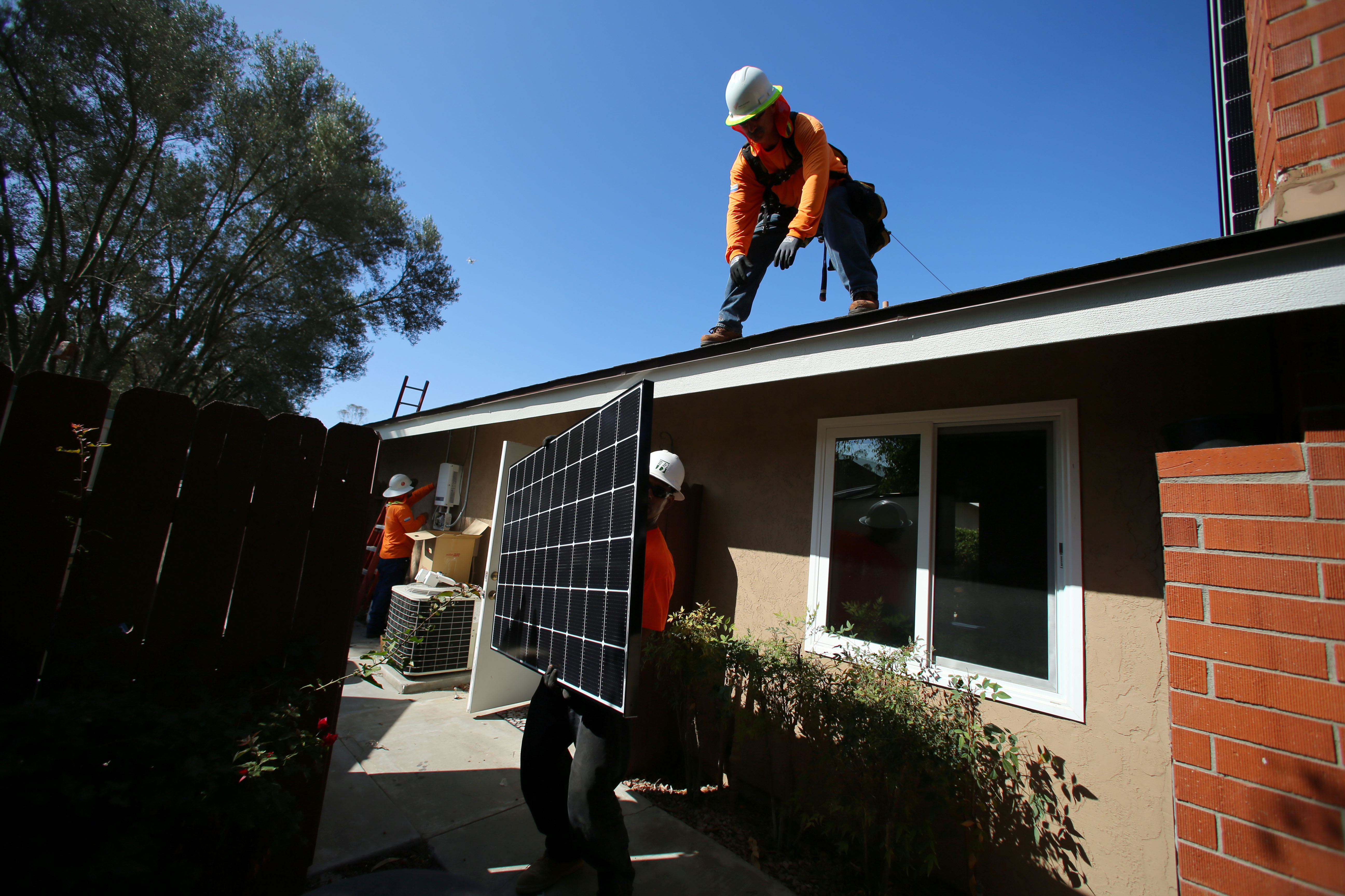 A man leans down off a roof to grab a solar panel being handed to him.