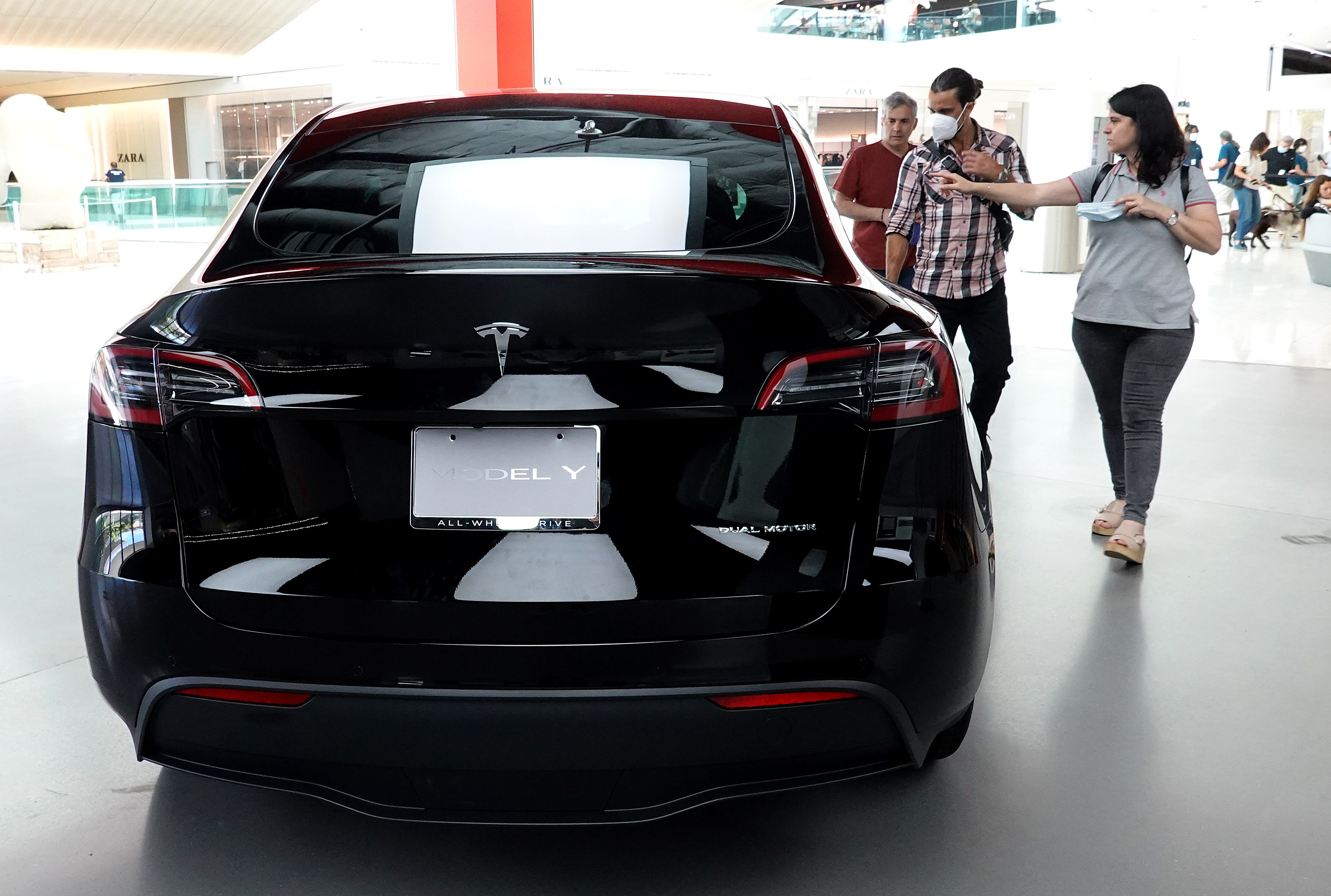 People inspect a Tesla Model Y electric vehicle in a showroom.