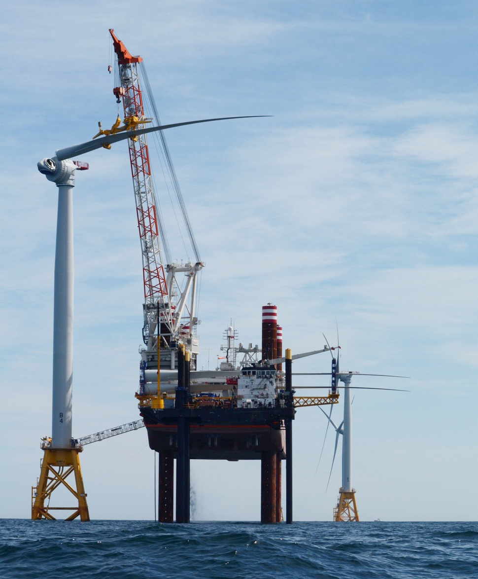 A crane extends into an offshore wind turbine under construction in the middle of the ocean.