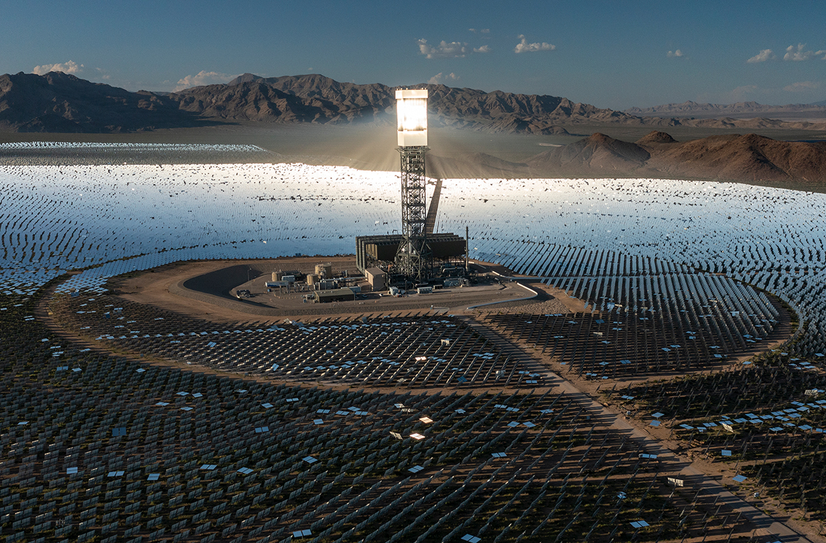 An aerial view of a tall bright boiler tower surrounded by mirrors in the Mojave Desert.