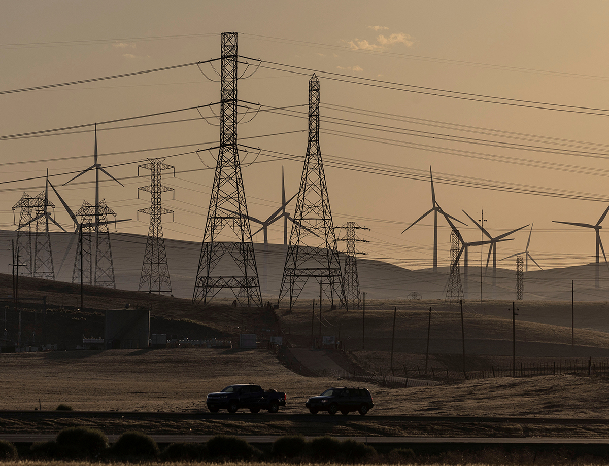 A field of power lines and windmills extend across an arid landscape.
