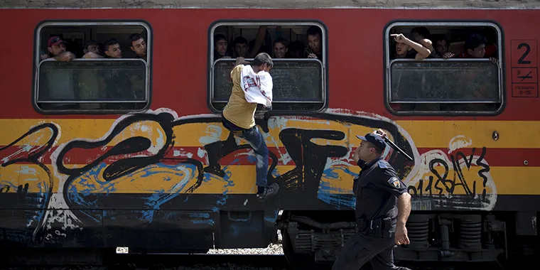 A policeman tries to stop a migrant from boarding a train through a window at Gevgelija train station in Macedonia, close to the border with Greece, on August 15, 2015.