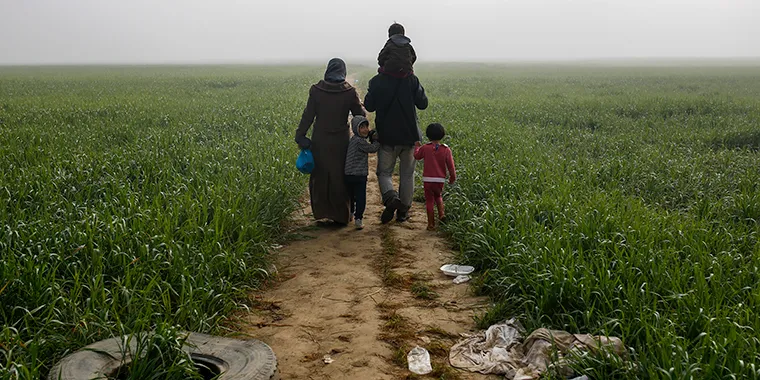 A family walks through a field at a makeshift camp for migrants and refugees at the Greek-Macedonian border near the village of Idomeni, Greece, on April 4, 2016.