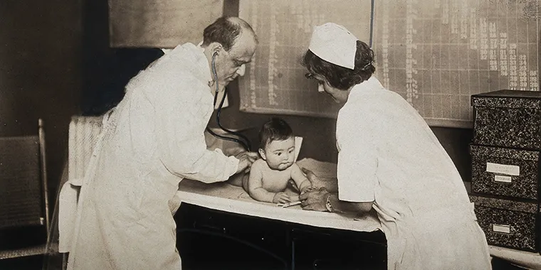 A baby is examined by a nurse and a doctor with a stethoscope at a state baby clinic in Pennsylvania, circa 1925.