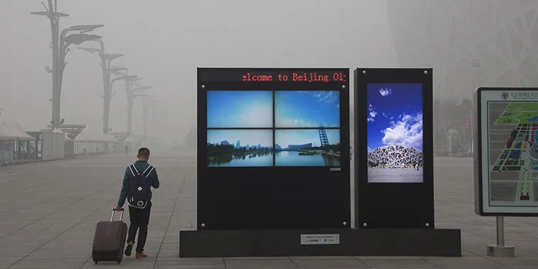 A man pulls his luggage past electronic screens showing the Olympic Green park under blue skies, near the National Stadium, or the Bird’s Nest, amid heavy smog in Beijing, China, on December 1, 2015.