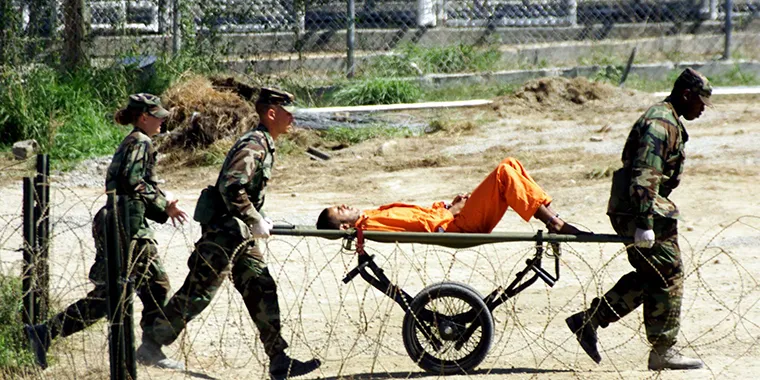 Military Police at Guantanamo Bay bring an injured detainee to an interrogation room for questioning, on February 2, 2002. 