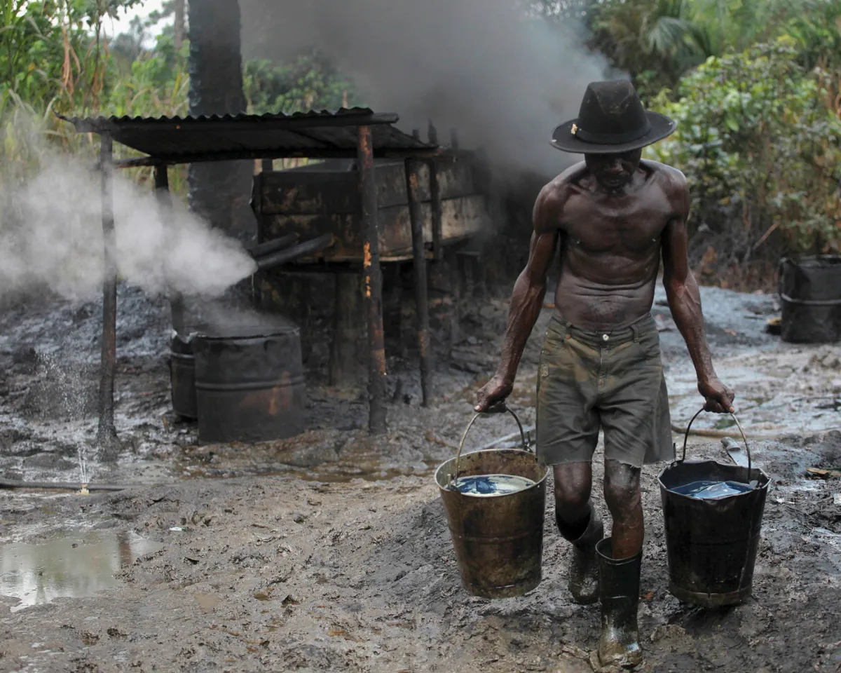 A photo showing a man carrying buckets of oil at an illegal refinery where stolen crude is processed, in Bayelsa, Nigeria on November 27, 2012.