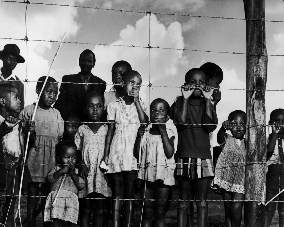 A photo showing children looking past a fence marking the boundary of a township designated for Black South Africans in Johannesburg, South Africa on April 21, 1950.