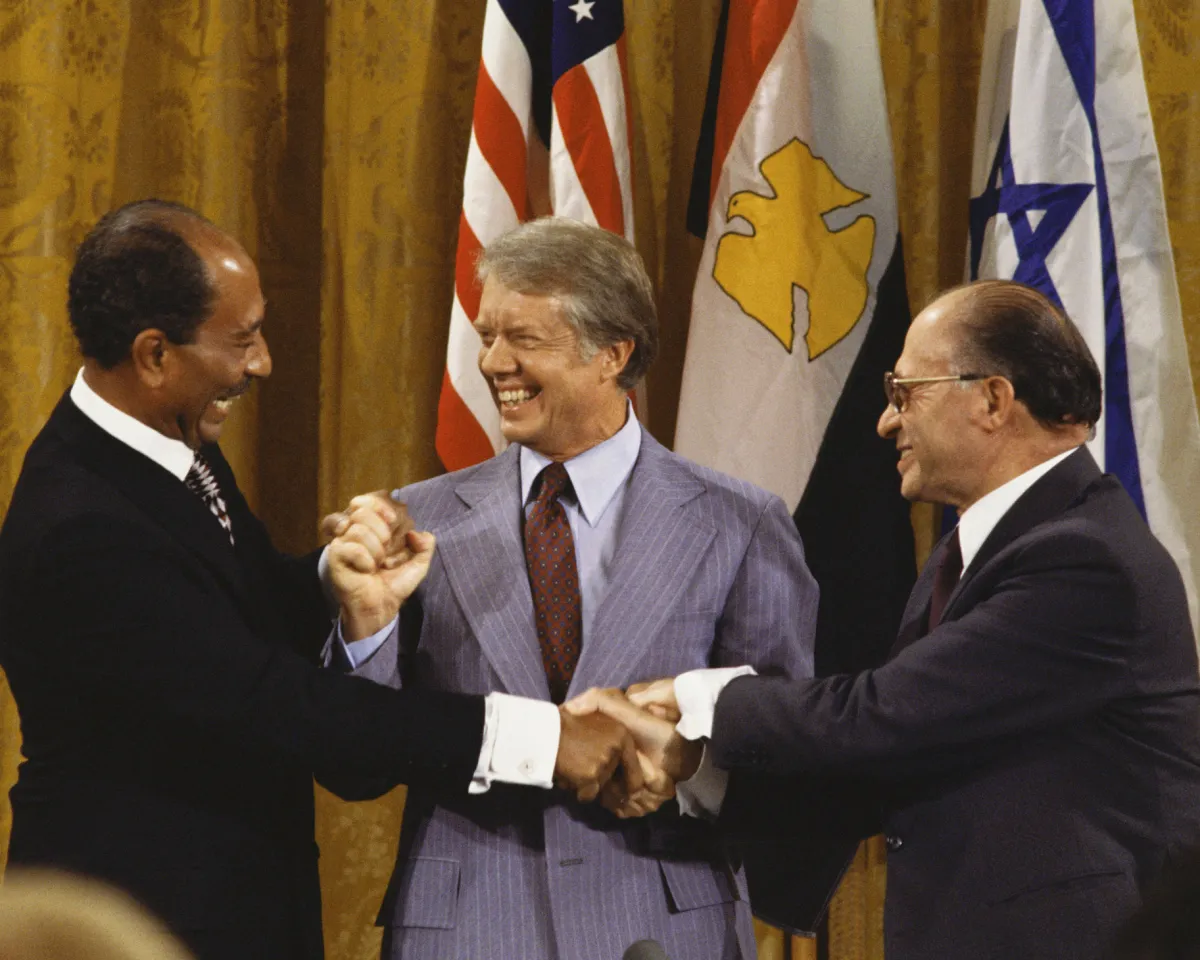 A photo of Egyptian President Anwar Sadat, U.S. President Jimmy Carter, and Israeli Prime Minister Menachem Begin joining hands after the Camp David Accords on September 18, 1978 in Washington, DC.