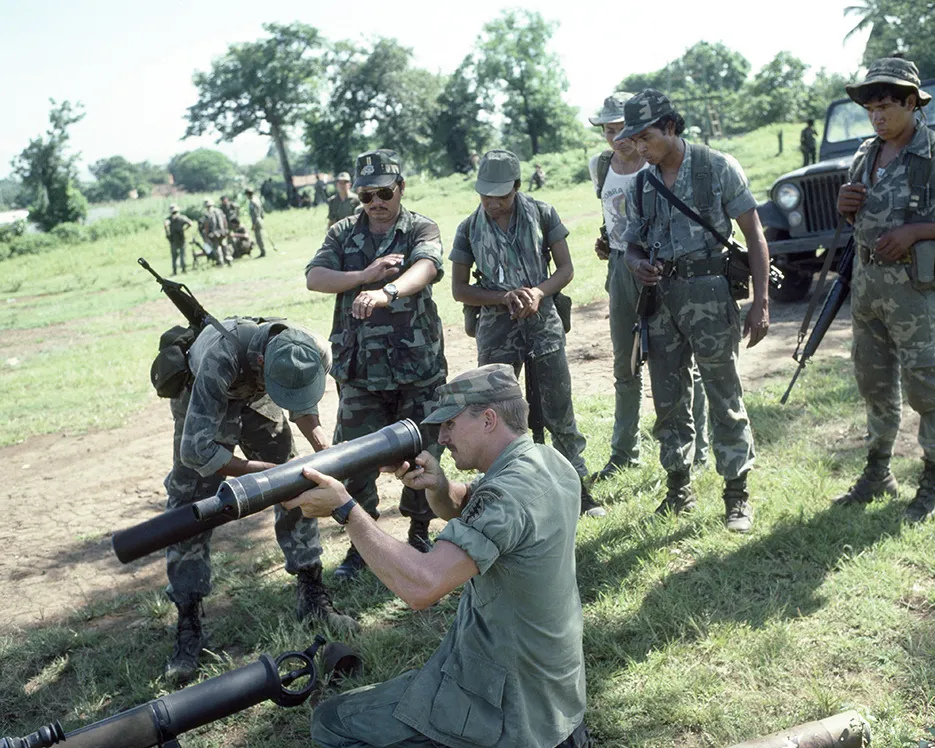 A photo showing U.S. Army trainer (center) examining part of a rifle during target practice with Salvadoran Army soldiers in August 1984 in San Miguel, El Salvador. 