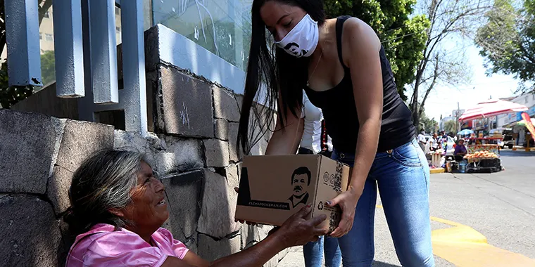 An employee of a clothing brand owned by Alejandrina Gisselle Guzman, daughter of the convicted drug kingpin Joaquin "El Chapo" Guzman, hands out a box with food, face masks, and hand sanitizers to an elderly woman.