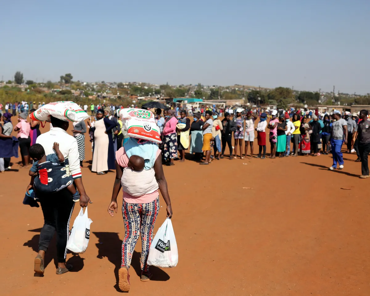 A photo showing women carrying bags of maize meal on their heads as people queue to receive food aid, amid the spread of the coronavirus disease (COVID-19) outbreak, at the Itireleng informal settlement in Pretoria, South Africa, on May 20, 2020.