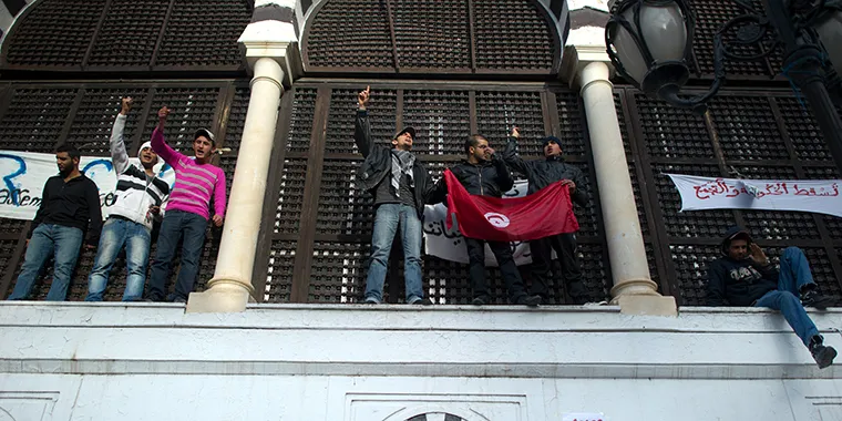 Protesters hold a flag of Tunisia as others shout slogans during a demonstration in a street of central Tunis on January 21, 2011.