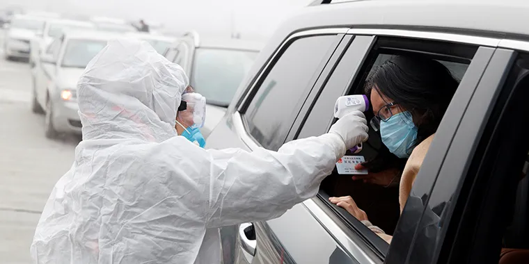 A medical worker in a protective suit checks the body temperature of a car passenger at a checkpoint outside the city of Yueyang in China after an outbreak of the coronavirus disease on January 28, 2020.