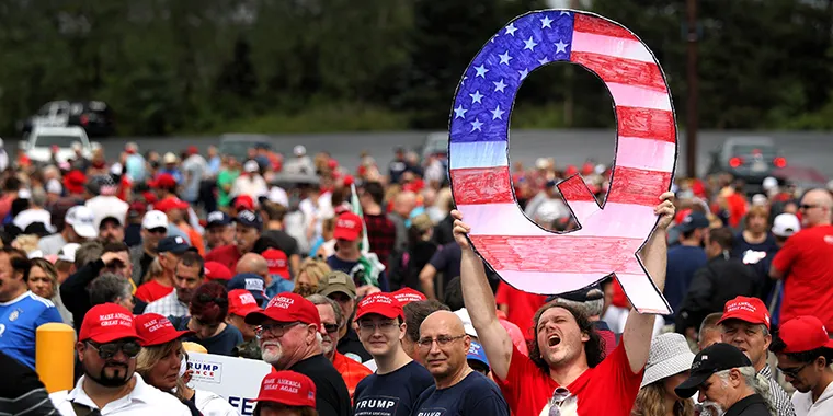 A man holds up a large "Q" sign while waiting in line to see then-President Donald J. Trump at his rally on August 2, 2018, in Wilkes Barre, Pennsylvania. "Q" represents QAnon, a conspiracy theory group.