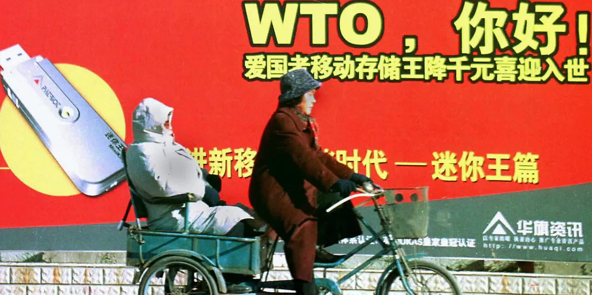 A Chinese couple on a tricycle pass a billboard welcoming the country's membership to the World Trade Organization (WTO), along a street in Beijing in 2001.