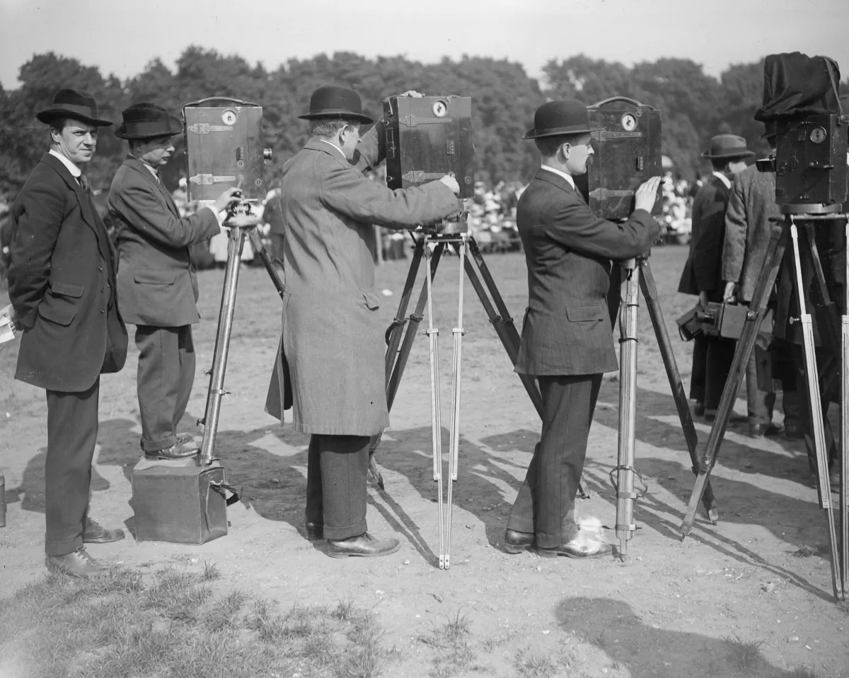 Several men film an event using old-fashioned hand-crank film cameras.