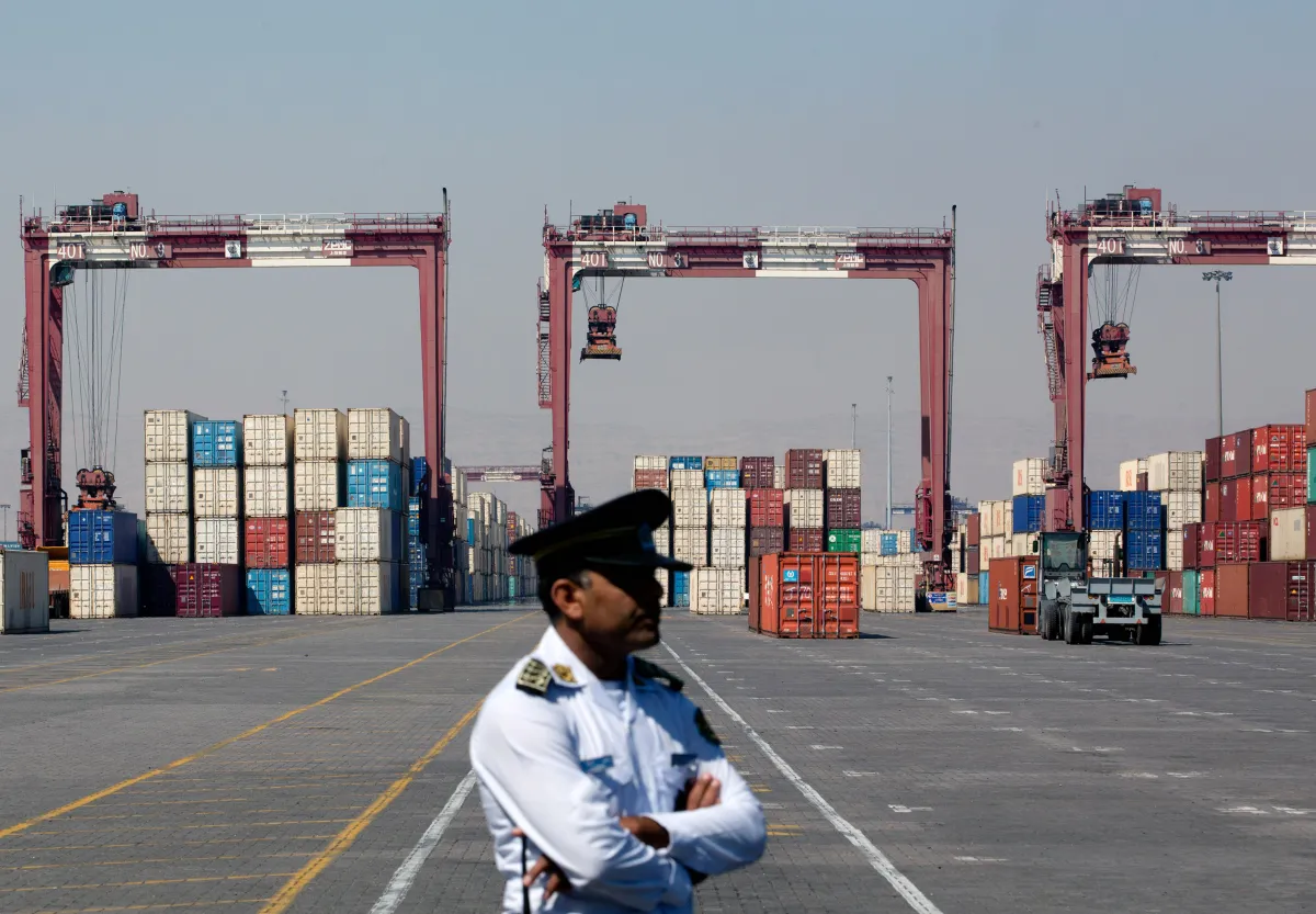 Security officer standing watch in front of shipping containers and machinery at a port.