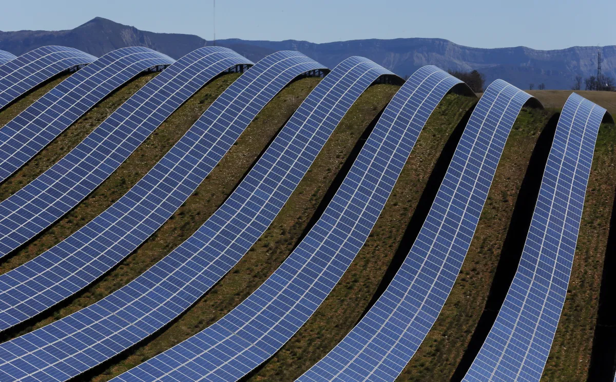 Rows of solar panels cover a green hill in France.
