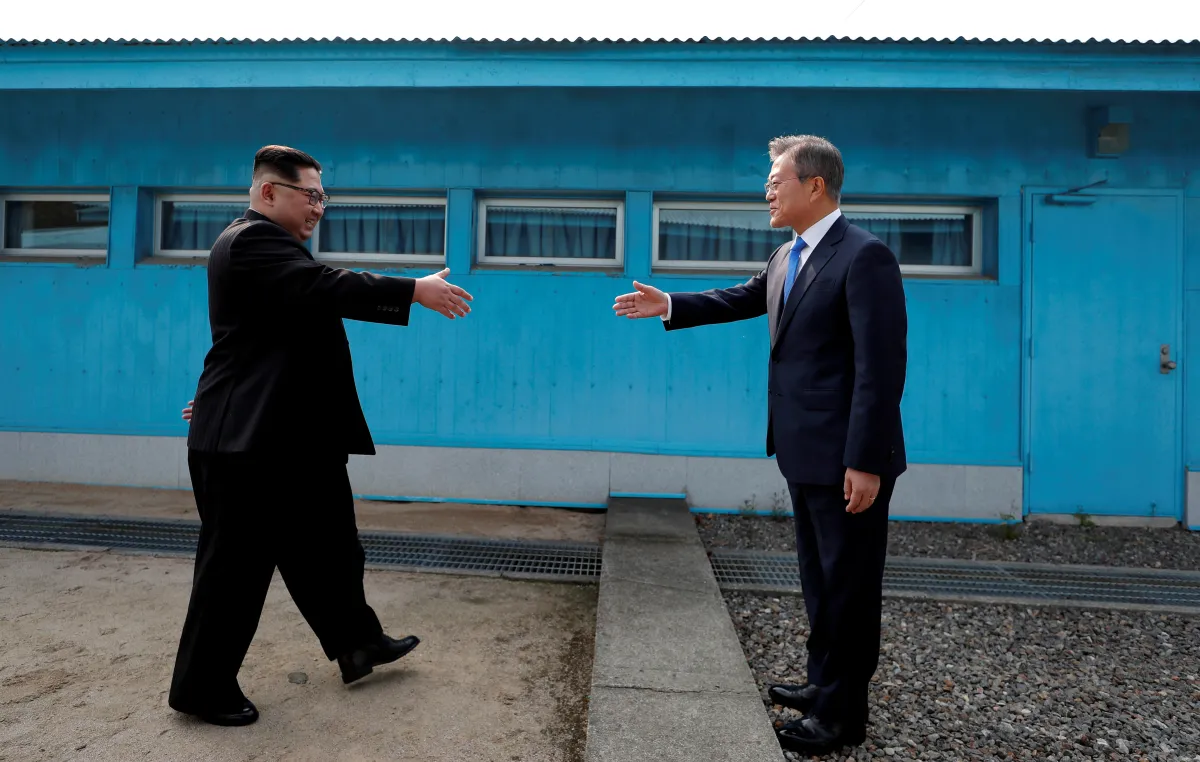 North Korean and South Korean leaders walking towards each other with arms extended for a handshake.