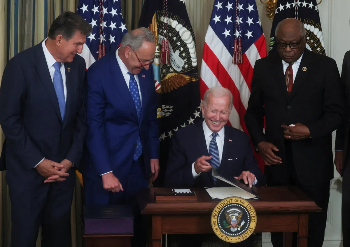 Biden signs inflation reduction act at a table as democratic congressional leaders watch next to him.