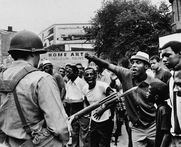 A man gestures with his thumb down at an armed National Guard service member, at a protest during the Newark riots in New Jersey, on July 14, 1967.