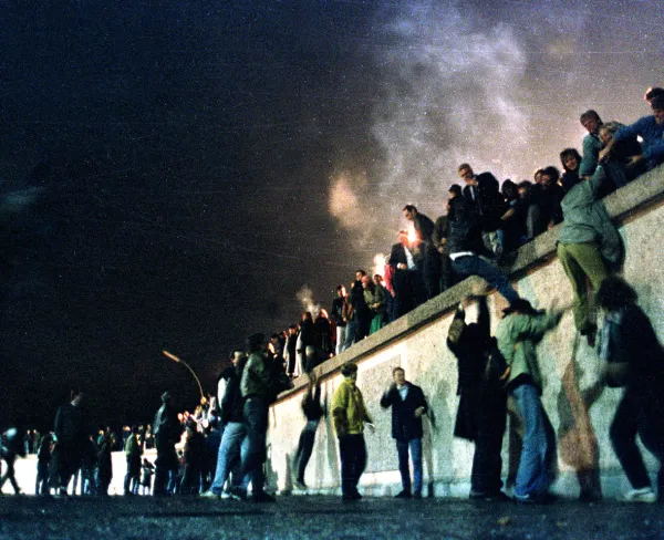 People from East Germany climb the Berlin Wall at the Brandenburg Gate after the opening of the East German border was announced, on November 10, 1989.
