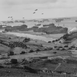 U.S. landing ships bring cargo ashore as barrage balloons float overhead to protect the ships and trucks head inland on one of the invasion beaches in Normandy in June 1944.