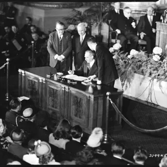 Secretary of State Dean Acheson signs the treaty on April 4, 1949. President Harry Truman and Vice President Alben Barkley are standing next to him.