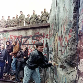 A demonstrator pounds away the Berlin Wall as East Berlin border guards look on from above the Brandeburg Gate on November 11, 1989.