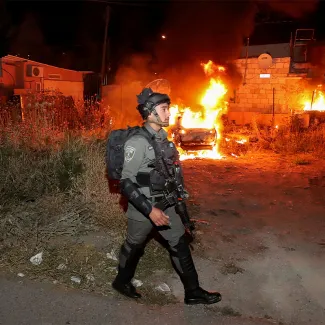 An Israeli border policeman walks as a car belonging to Jewish settlers burns amid tension over the possible eviction of several Palestinian families from homes on land claimed by Jewish settlers in East Jerusalem on May 6, 2021.