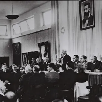 David Ben-Gurion, flanked by the members of his provisional government, reads the declaration of independence in the Tel Aviv Museum Hall.